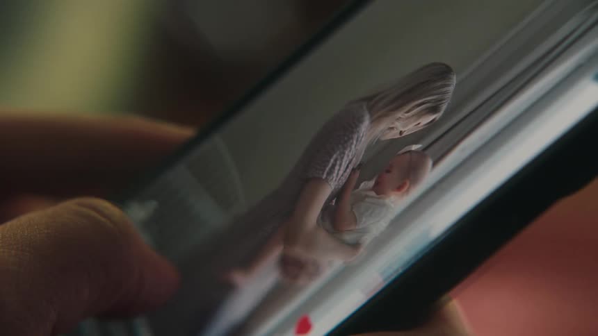 A woman holding a baby in a video on a cell phone screen