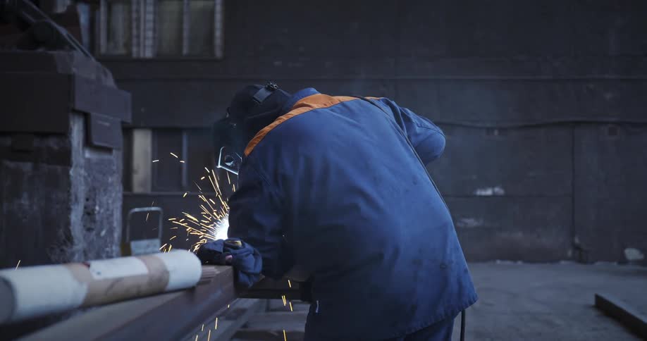 Man with his back leaning on a table using a tool that produces sparks and smoke