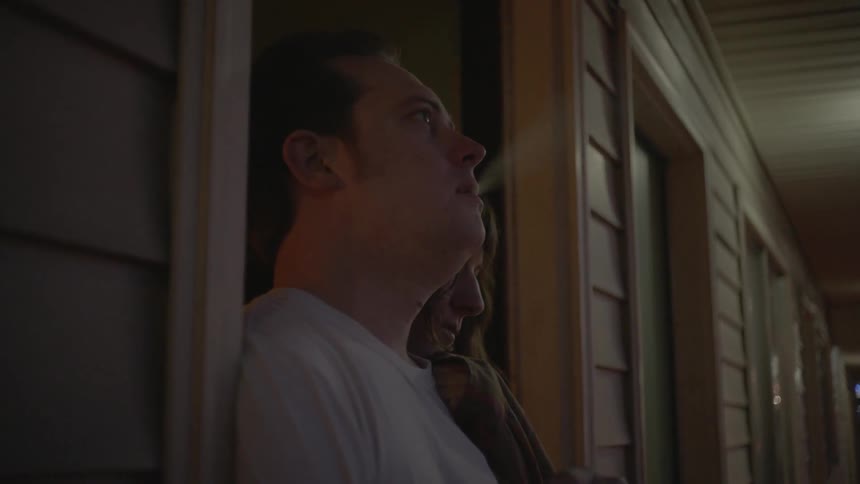 A couple stands in a doorway while the man smokes a cigarette