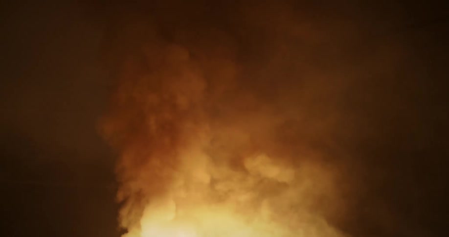 Smoke billows upwards from a fire that is burning at nighttime