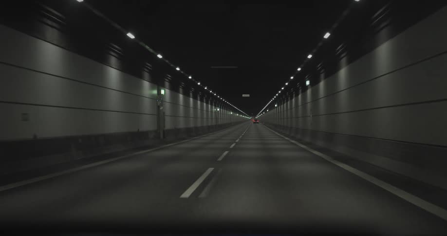 Cars travel on a road through a tunnel with lights on the ceiling