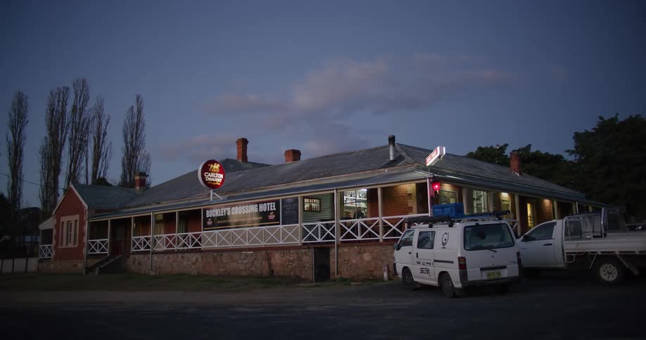 A view of the outside of a restaurant with a van and a small truck parked outside on a darkening day