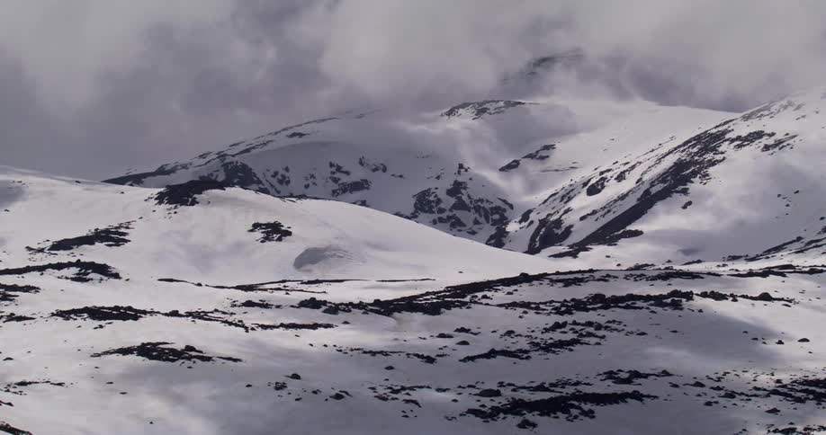 Low lying clouds cast shadows across snow covered mountains