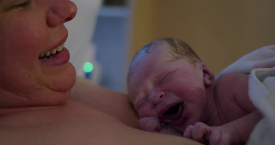 A newborn baby crying on its mothers chest