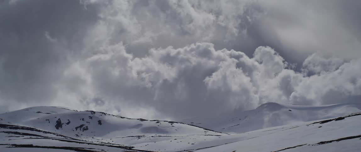 Thick clouds pass over snow covered mountains