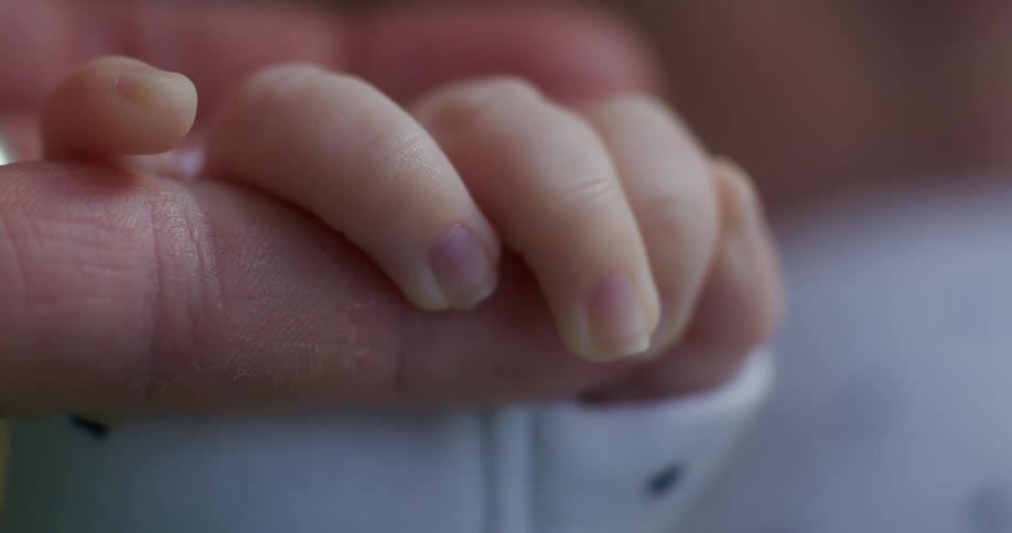 A baby holds her mother's hand