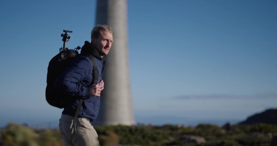 Man with a backpack and a tripod walking on a hill in a blue sky natural environment during the day