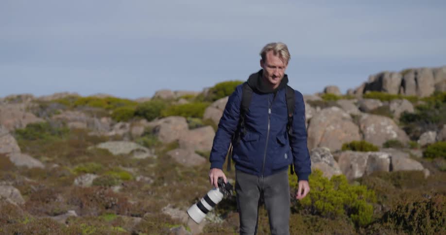 Man photographer walking with his professional camera in the middle of a hill with rocks