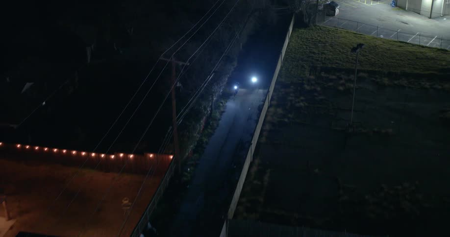 Two motorcycles drive down streets at night
