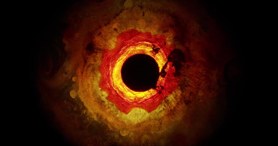 A dark circle surrounded by flowing shimmering yellowish liquid