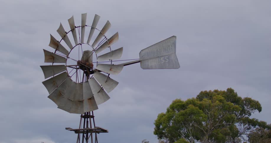 A farming windmill stands nearly motionless under a cloudy sky