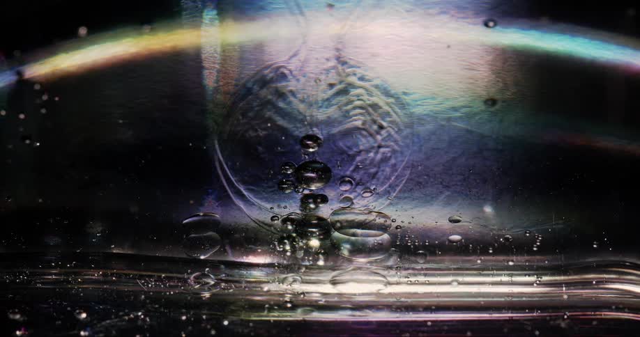 Bubbles float within a viscous liquid with abstract light shining behind it