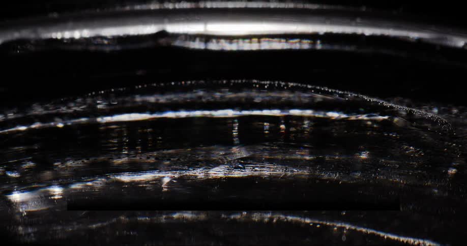 Circular patterns and ripples on a dark oily surface reflecting light
