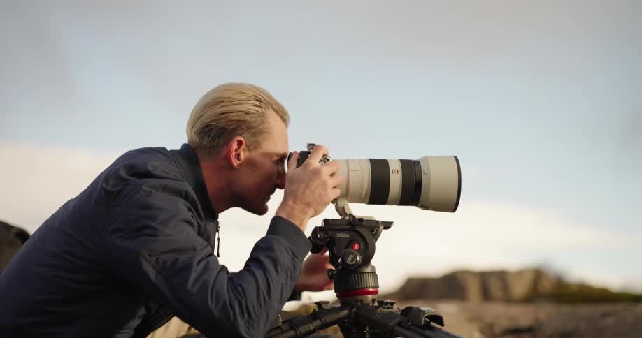 Male photographer adjusts camera with telephoto lens while taking pictures outdoors