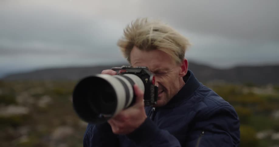Man taking photo with his professional camera with zoom lens in an outdoor environment in nature with a lot of wind
