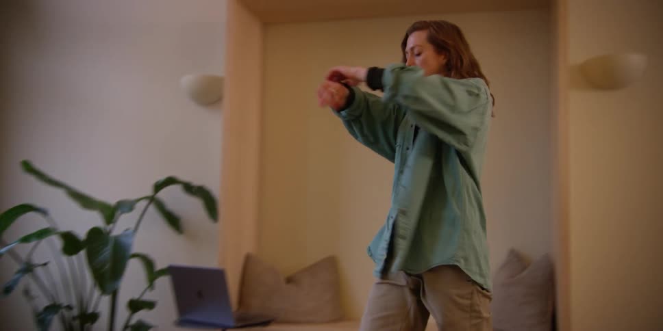 A red-headed woman is stretching with smooth dance motions in her living room.