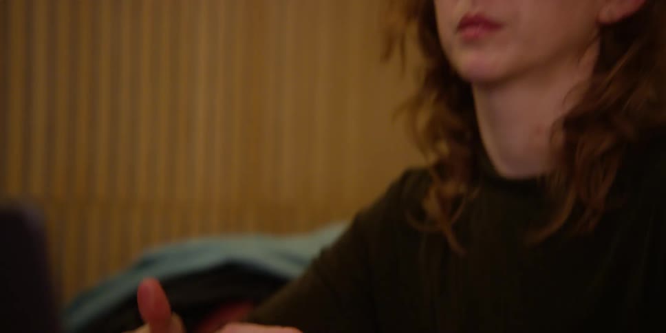 A fair-skinned woman with red hair has her head in her hand as she studies dance movements on her laptop and acts them out with her hands.