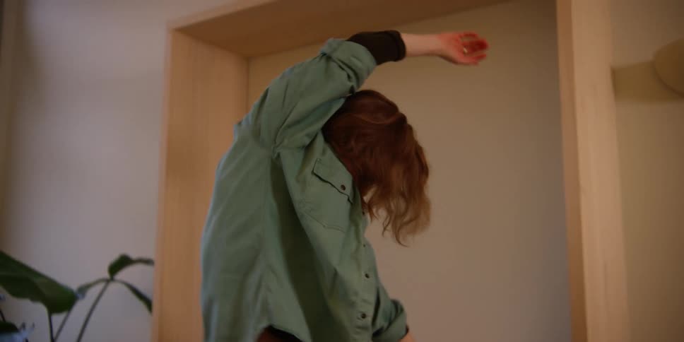 A fair-skinned, red-headed woman does a stretching routine in preparation to dance.