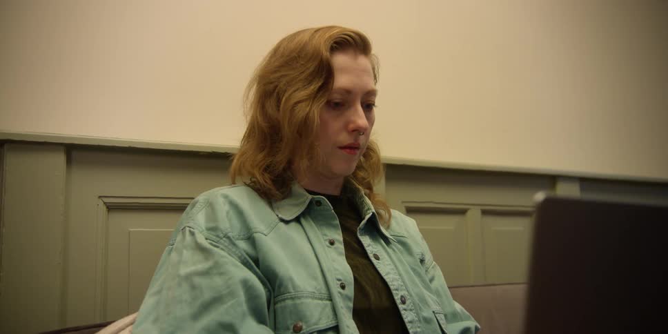 A fair, red-headed woman sitting concentrating on the screen as she types and works on a laptop