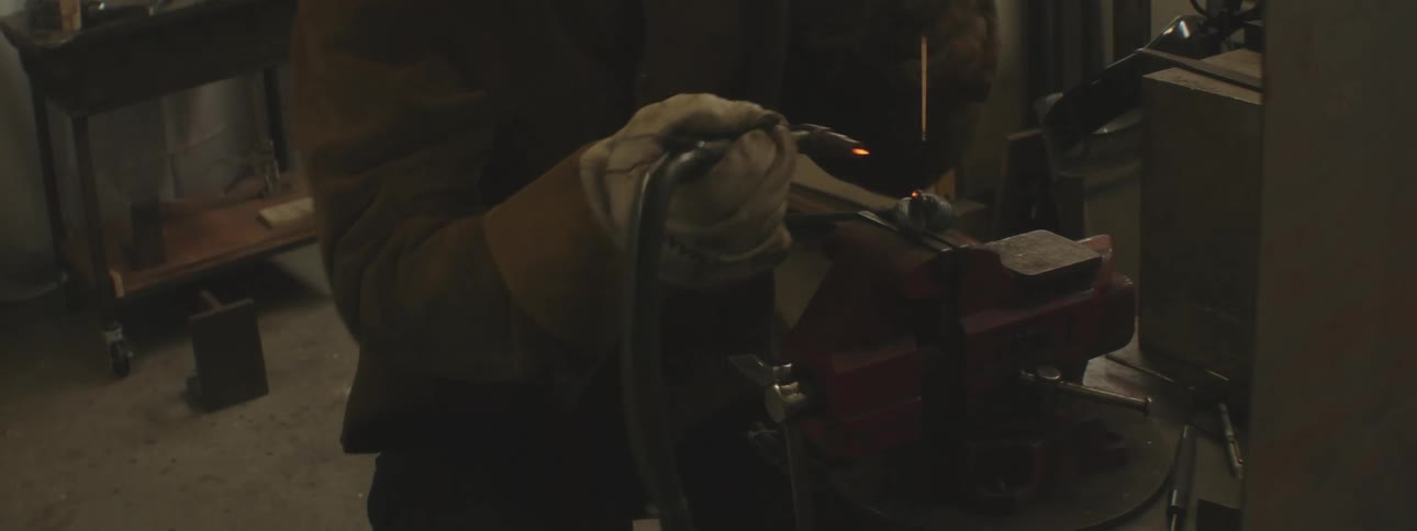 A person is welding with sparks flying in a dimly lit industrial setting