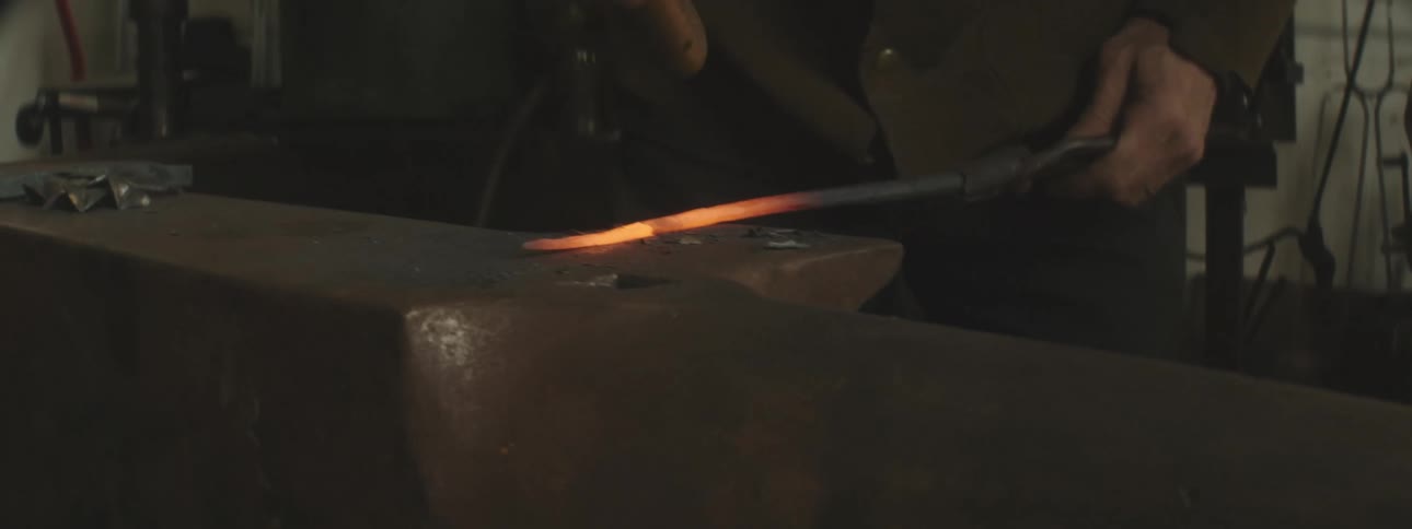 A man is hammering a hot rod on the anvil