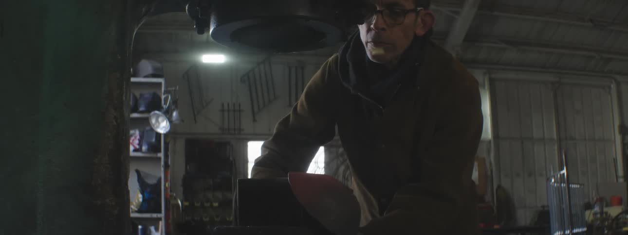 A man is using a machine to hammer and form metal