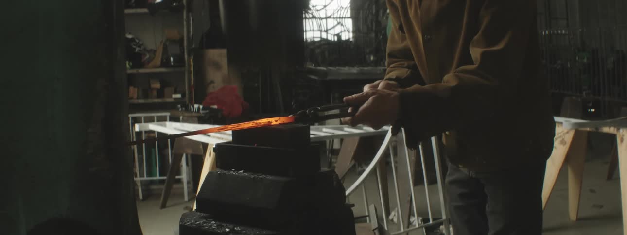 Man holding a rod that was taken from a furnace and putting into a forging understanding machine