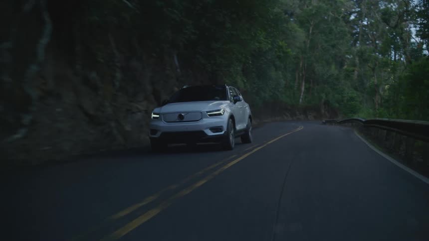 A white car travels around a curve on a forested mountain road