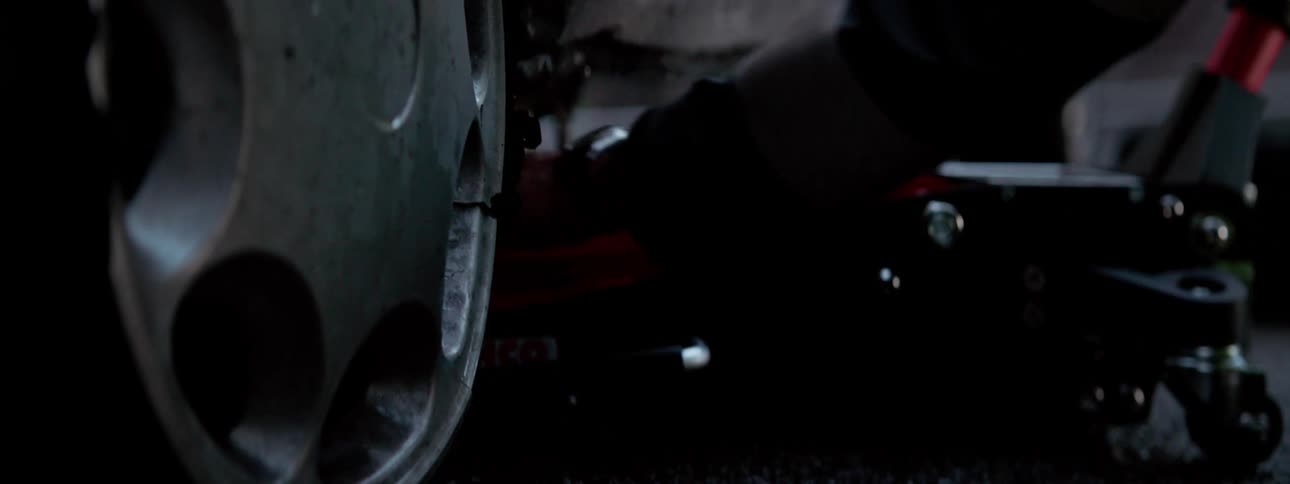 A person takes a hydraulic jack and places it under a car and begins to lift it