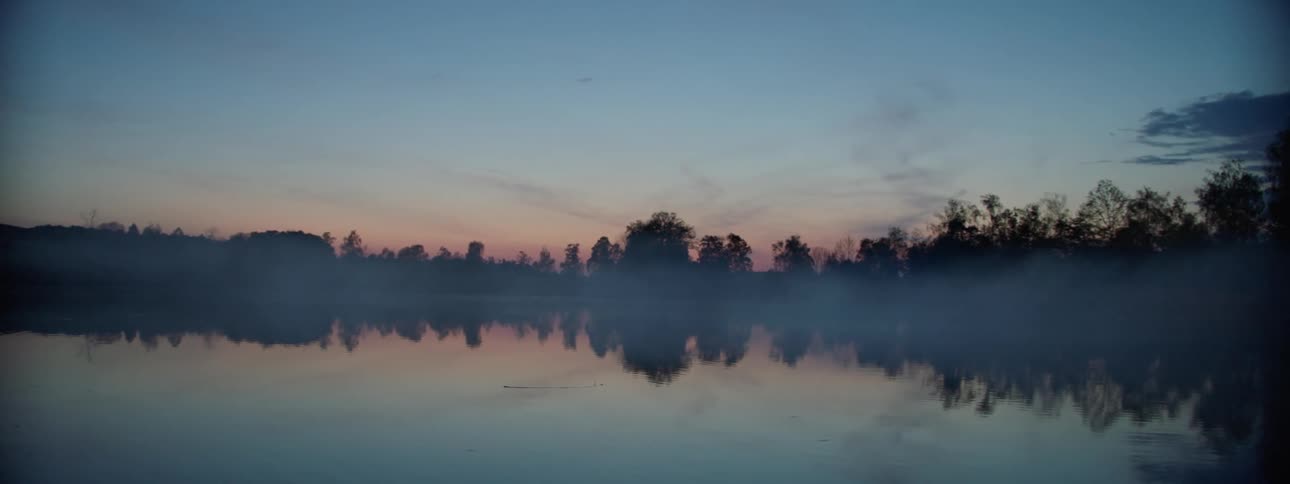 Water reflects trees on shore silhouetted against a red horizon