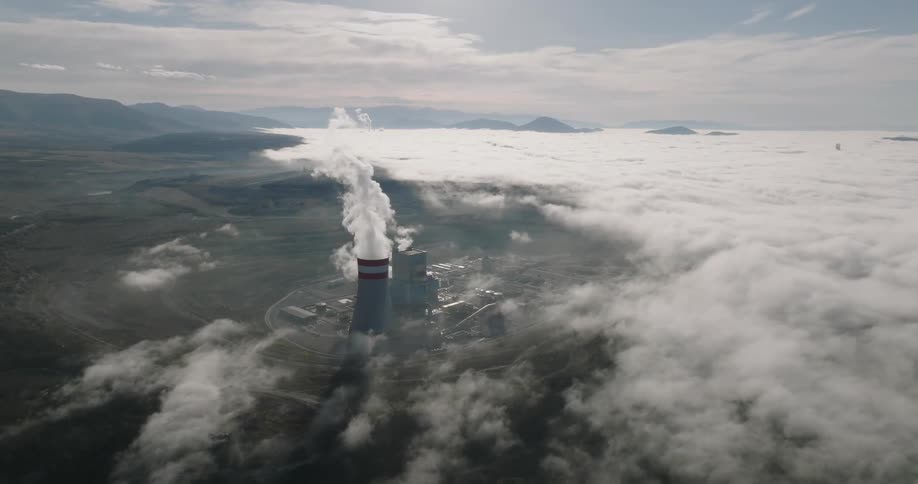 Smoke rises from energy plant situated near foggy shore