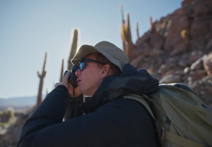 A hiker in the desert takes a photo of the scenery with a professional camera then walks off on a dirt path