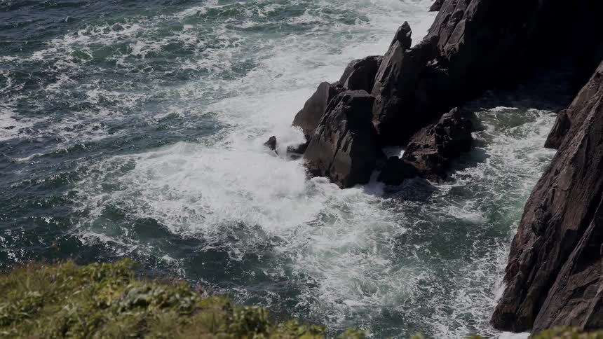 Sea waves crash on the beachs rocky shore during the day