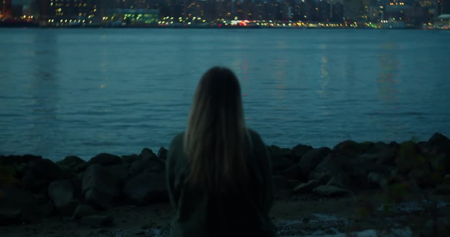 Woman watches the flowing river with a lively metropolis behind it