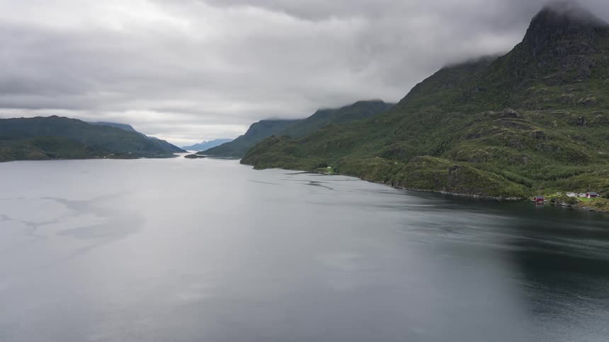 Multiple clusters of buildings are separated by mountainous terrain on shore under an overcast sky