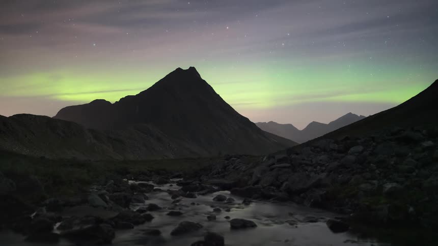 Landscape of rocks on a dry river with mountains around and the sky like aurora borealis