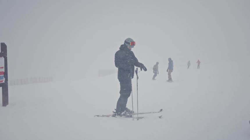A group of people on a mountain wearing skis during a snowstorm