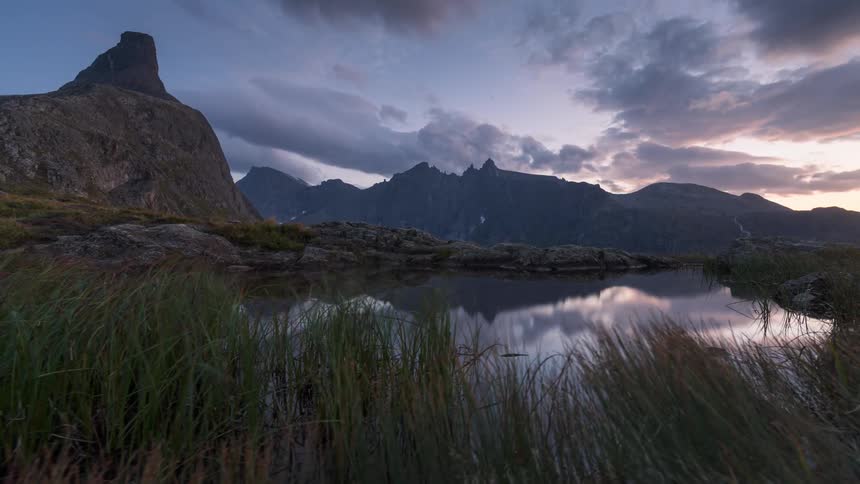 Small lake reflects clouds and surrounding mountains on a misty day