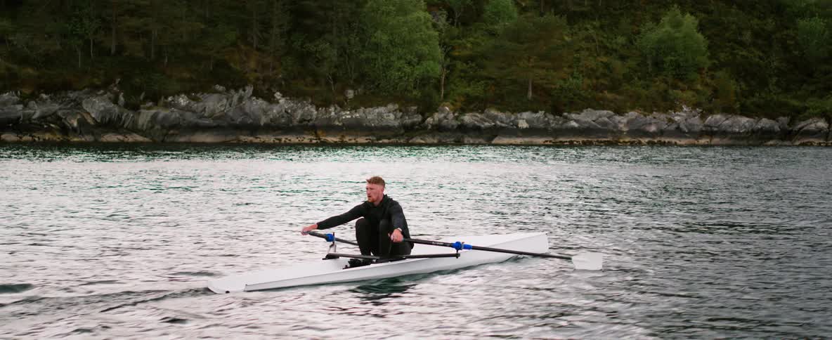 A man paddles a kayak on a lake near the mountainous coast