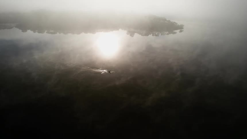 Epic aerial of a solitary rowing journey in the early dawn with ethereal clouds