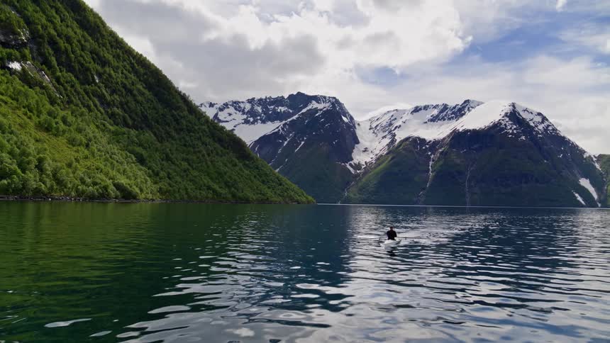 Majestic landscape with a man rowing alone in the Norwegian fjords surrounded by snowy peaks