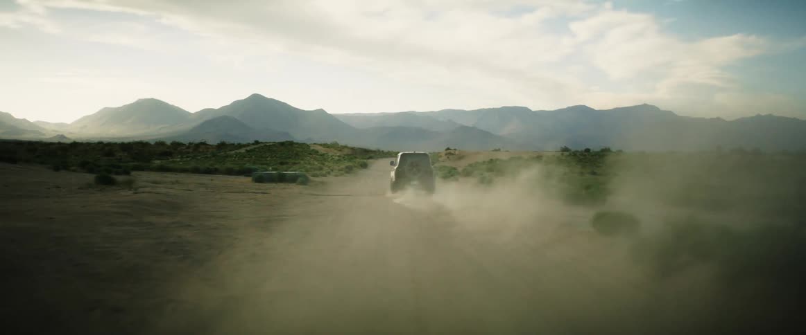 Suv makes a hard right onto dusty desert road driving towards mountains