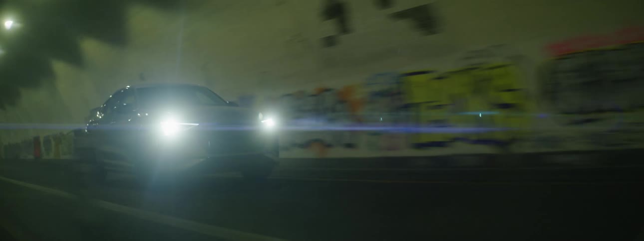 A silver car driving through a tunnel in the city at night