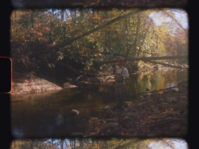 A man standing next to a stream surrounded by trees