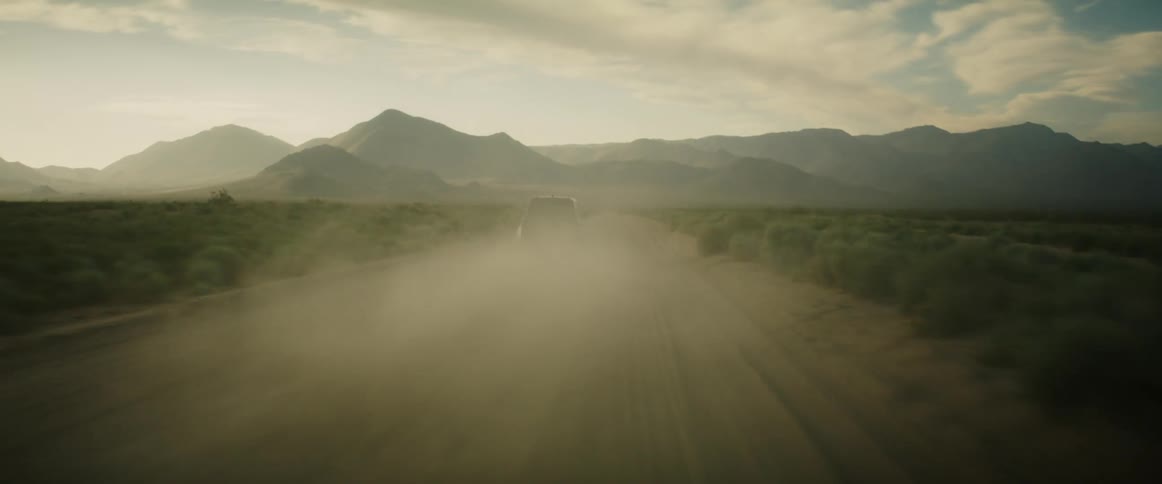 A vehicle drives down a desert road