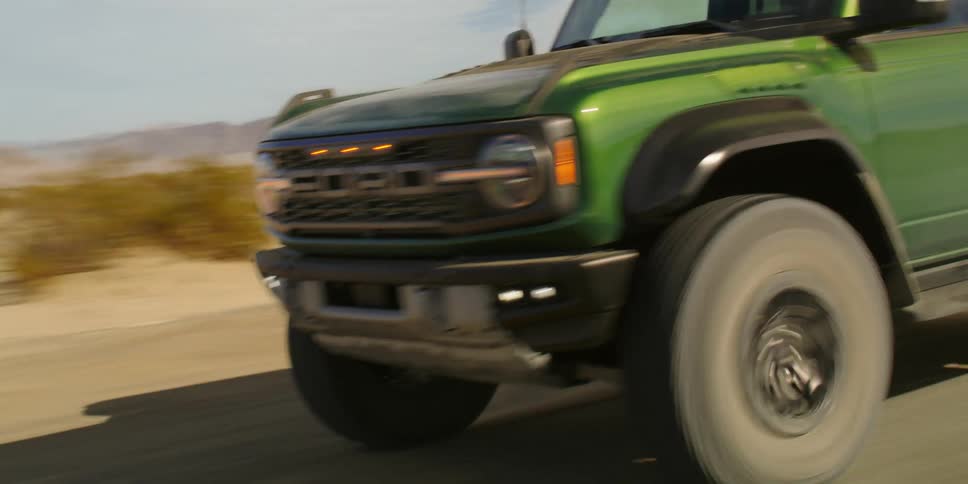 Green ford bronco drives through desert landscape during the day