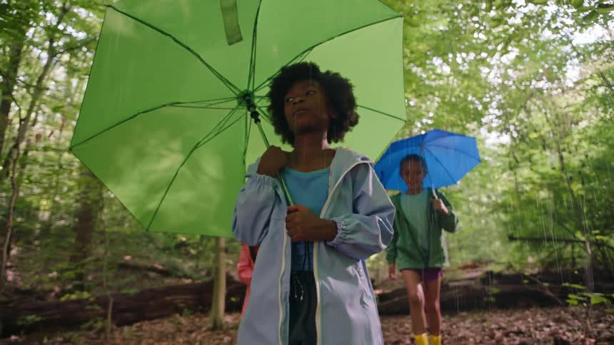 Three kids walk through a forest during a rain shower