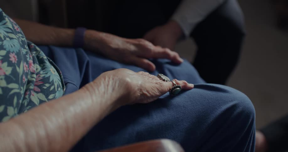 An elderly woman rests her hands on her legs