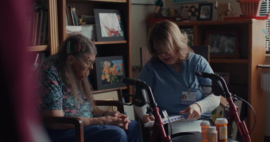 A nurse holds a pill container and speaks with a patient