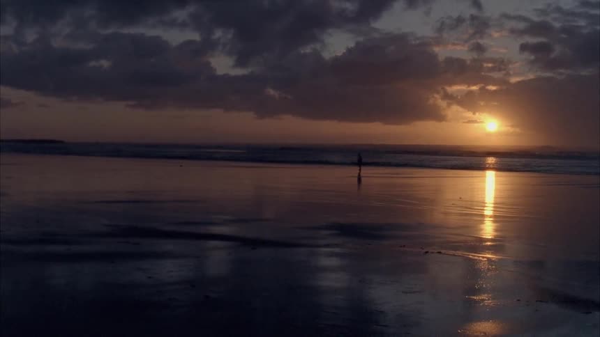 Someone running on the edge of the water on a beach at sundown